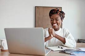 A lady smiling with her hands tightly closed and sitting behind a laptop