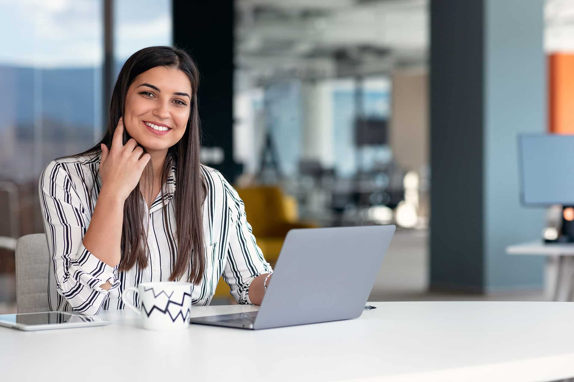A lady smiling and sitting behind a laptop.